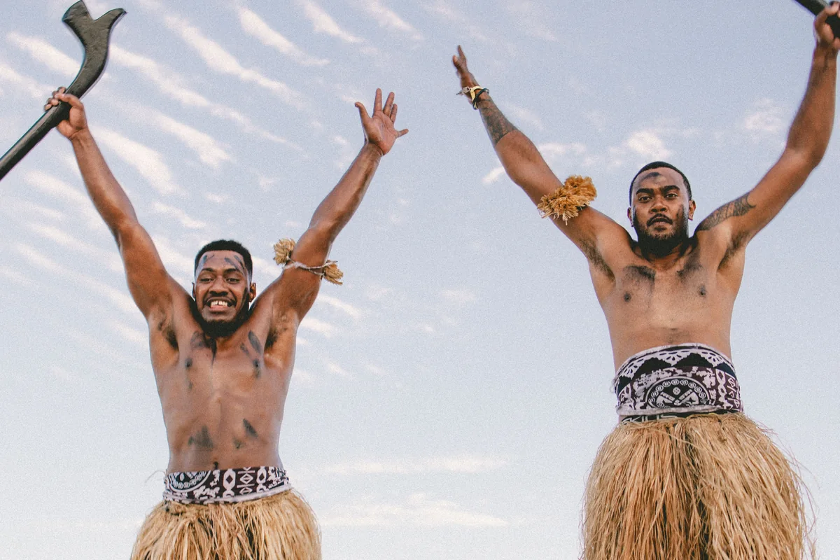Fijian men in traditional dress with a war club, arms raised, near Nadi, Fiji